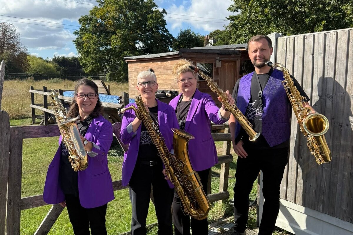 Swan Saxophone Quartet in purple jackets posing outdoors with their saxophones